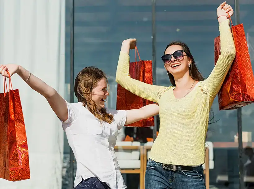 Two happy women holding large shopping bags outdoors